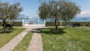 A pathway leading to a glass-enclosed area with benches and a view of the sea. - Il Professore: front lake apartment (Manerba del Garda)