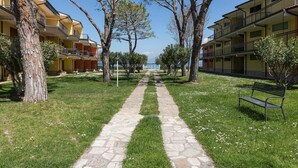 A pathway leading to a building with balconies, surrounded by trees and grass. - Il Professore: front lake apartment (Manerba del Garda)