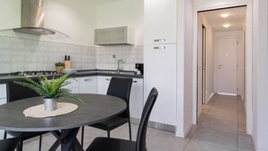 A modern kitchen with white cabinets, a stainless steel range hood, and a dining area with a round table and chairs. - Il Professore: front lake apartment (Manerba del Garda)