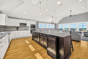 A spacious kitchen with white cabinets, a large island, and a view of the ocean. - Surfside Retreat Oceanfront  Home + Pets Stay Free! (Buxton)