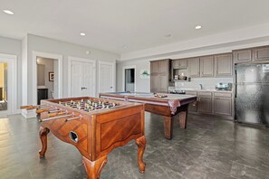 A spacious kitchen with two foosball tables, a refrigerator, and wooden cabinets.