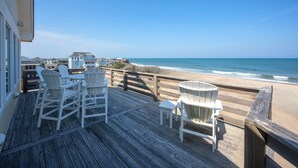 A wooden deck with white chairs and a table overlooking a beach.