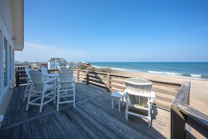 A wooden deck with white chairs and a table overlooking a beach. - Surfside Retreat Oceanfront  Home + Pets Stay Free! (Buxton)