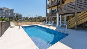 A rectangular swimming pool with a wooden deck and lounge chairs.