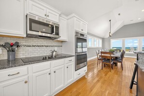 A modern kitchen with white cabinetry, stainless steel appliances, and a wooden dining area with a view.