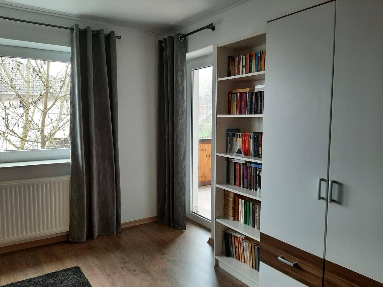 Una habitació amb una finestra gran, una estanteria i un armari.