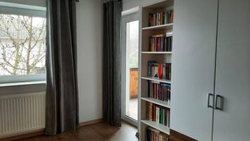 Una habitació amb una finestra gran, una estanteria i un armari.