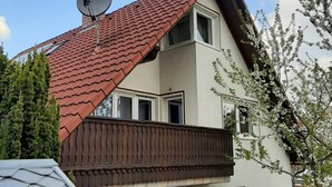 Une maison à deux étages, avec un toit recouvert de tuiles rouges, une antenne parabolique et un balcon.
