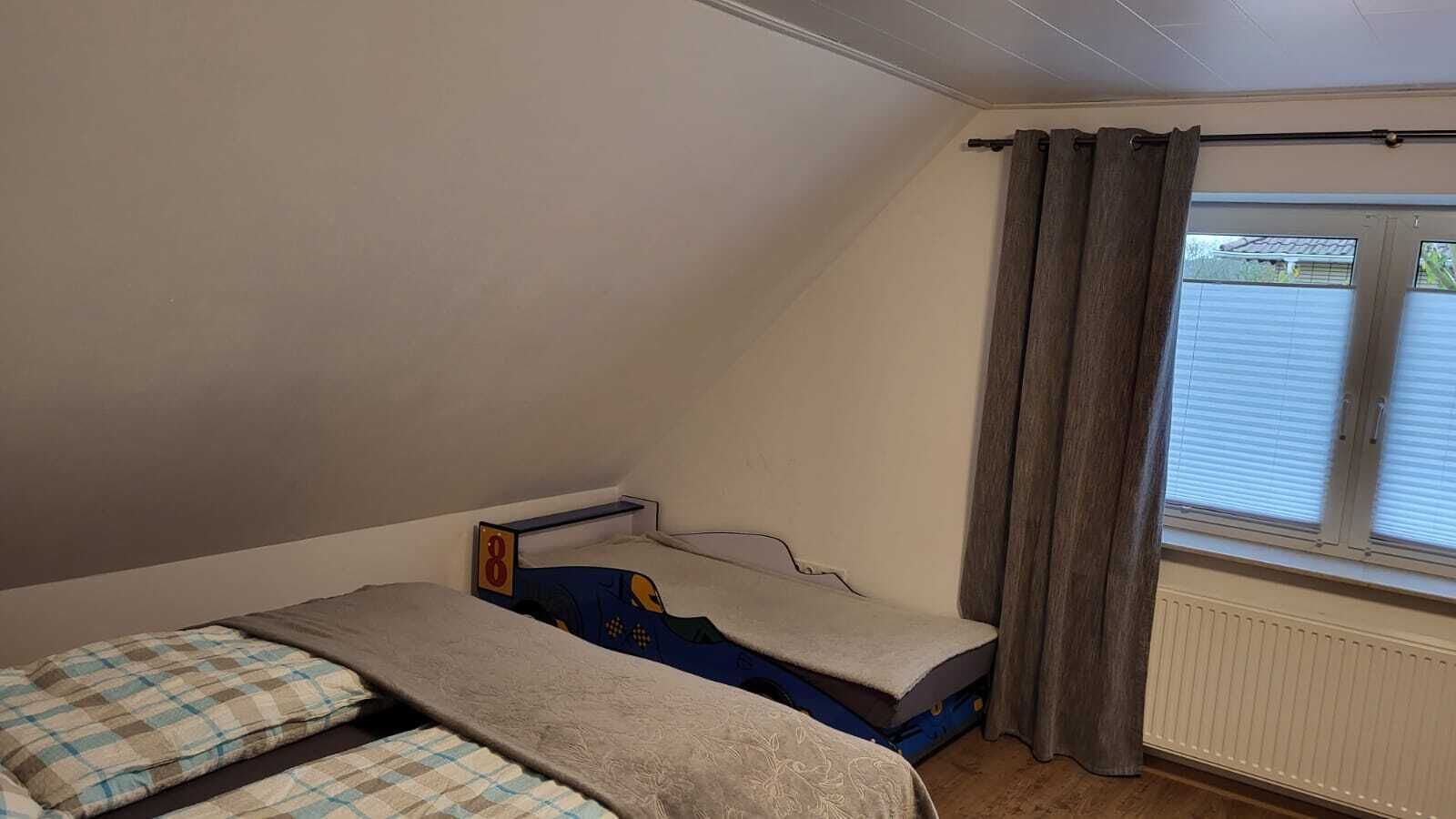 Et lille værelse med en enkeltseng, skråvæg, et vindue med persienner og en radiator.