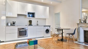 Eine moderne Küche mit weißen Schränken, einer Mikrowelle, einem Backofen und einer Waschmaschine. Es gibt einen Essbereich mit einem runden Tisch und Stühlen sowie einen Kamin.