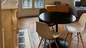 Ein Wohnzimmer mit einem runden schwarzen Tisch, weißen Stühlen, einem beigen Sofa, einem an der Wand befestigten Fernseher und einer großen Stehlampe.