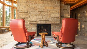 Two red chairs with a wooden table in front of a stone fireplace.
