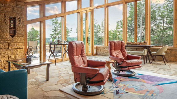 A spacious room with large windows, a stone wall, and leather chairs.