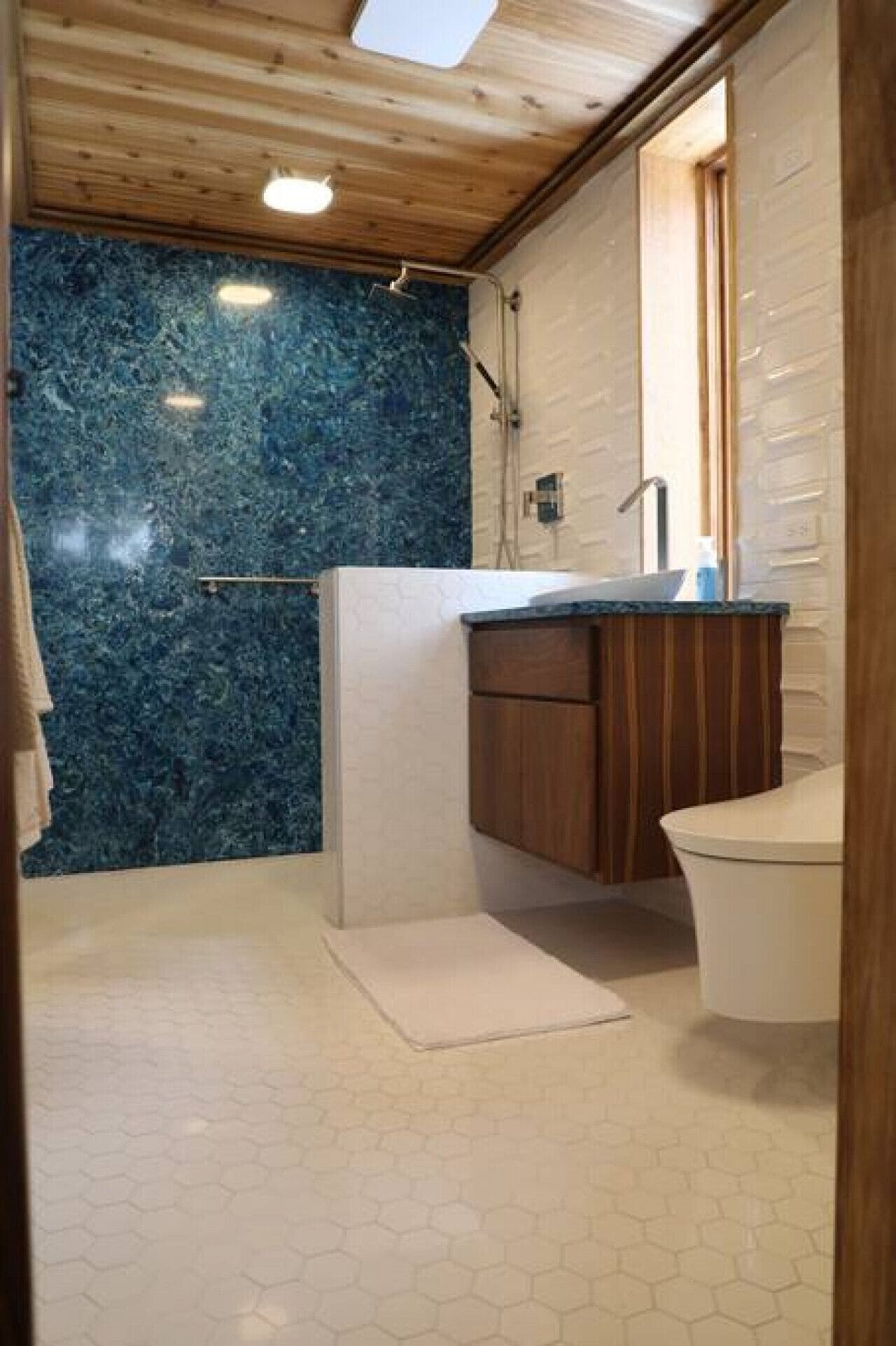 A bathroom with a wooden ceiling, a blue marble wall, a wooden vanity, and a white toilet.