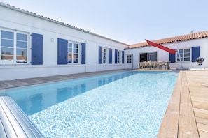 A swimming pool with a wooden deck, a barbecue area, and a building with blue shutters. - Old village school with swimming pool (Saint-Pierre-d'Oléron)