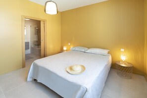 A neatly made bed with a hat on it, a bedside lamp, and a door leading to a bathroom. - Old village school with swimming pool (Saint-Pierre-d'Oléron)