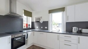 A modern kitchen with white cabinets, a black countertop, a stainless steel range hood, and a window with a view. - Whisky Cottage, Great location, spacious, sleeps 6 (Inverness)