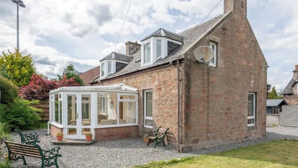 A traditional stone house with a conservatory, a gravel driveway, and a bench. - Whisky Cottage, Great location, spacious, sleeps 6 (Inverness)
