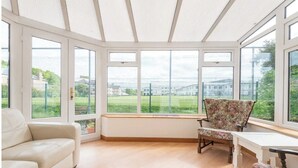 A conservatory with a white bench, a floral armchair, and a sofa. - Whisky Cottage, Great location, spacious, sleeps 6 (Inverness)
