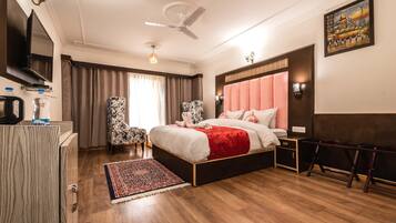 Habitación de hotel con cama, escritorio con televisor, silla, alfombra y ventilador de techo.