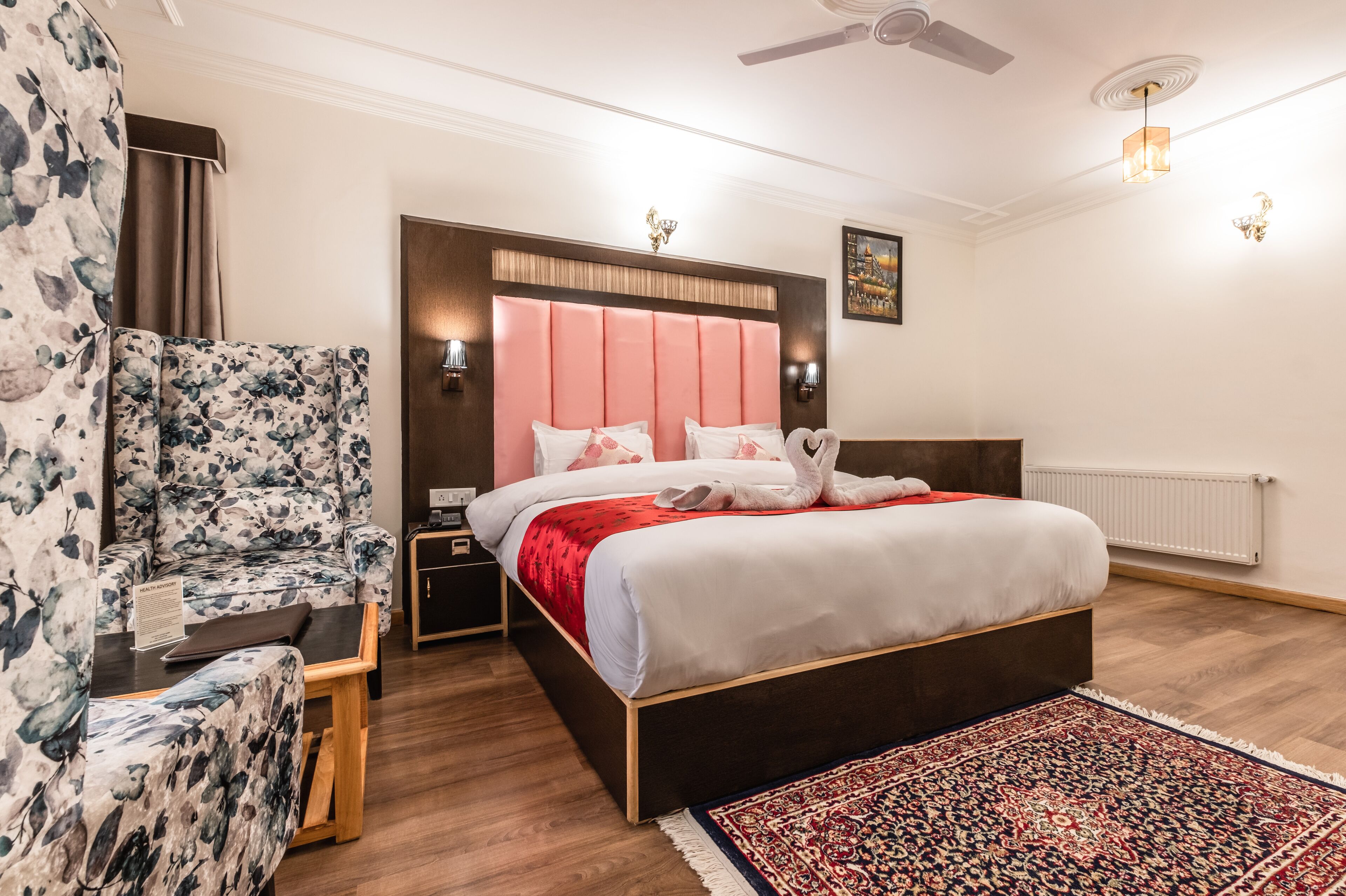 A bedroom with a large bed, a chair, a nightstand, a wall-mounted lamp, and a ceiling fan.