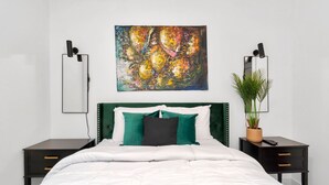 A modern bedroom with a white bed, green and black pillows, a green headboard, a large abstract painting, two bedside tables with lamps, and a potted plant. - ✵The Allure✵| Houston Hidden Gem - NRG/Med Center (Houston)