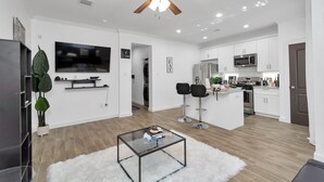 A modern kitchen with white cabinets, a microwave, and a stove. There is a dining area with two black bar stools and a glass coffee table. - ✵The Allure✵| Houston Hidden Gem - NRG/Med Center (Houston)