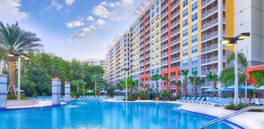 Ein Hotel mit Swimmingpool, umgeben von Palmen und Liegestühlen.