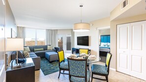 A modern hotel room with a sofa, dining table, chairs, a TV, and a balcony with a view. - 1 Bdr Condo w/ Full Kitchen min. from Disney and Universal! (Kissimmee)