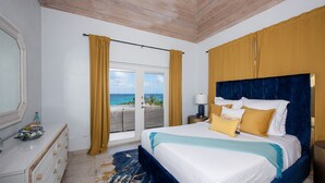 Een slaapkamer met een groot bed, een dressoir, een nachtkastje en uitzicht op de oceaan.