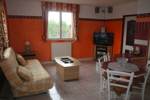 A compact living space with a sofa, a small table, a TV, and a dining area with chairs. - Seasonal rental of air-conditioned gîtes, swimming pool (Caux)