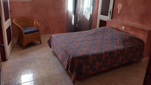 A bedroom with a bed, a wicker chair, a window, and a door. - Seasonal rental of air-conditioned gîtes, swimming pool (Caux)
