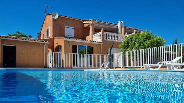 A swimming pool with clear blue water, a white fence, and a building with balconies and a satellite dish. - Seasonal rental of air-conditioned gîtes, swimming pool (Caux)