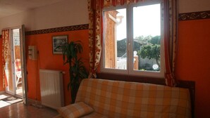 A room with a checkered sofa, a radiator, a potted plant, and a window with curtains. - Seasonal rental of air-conditioned gîtes, swimming pool (Caux)