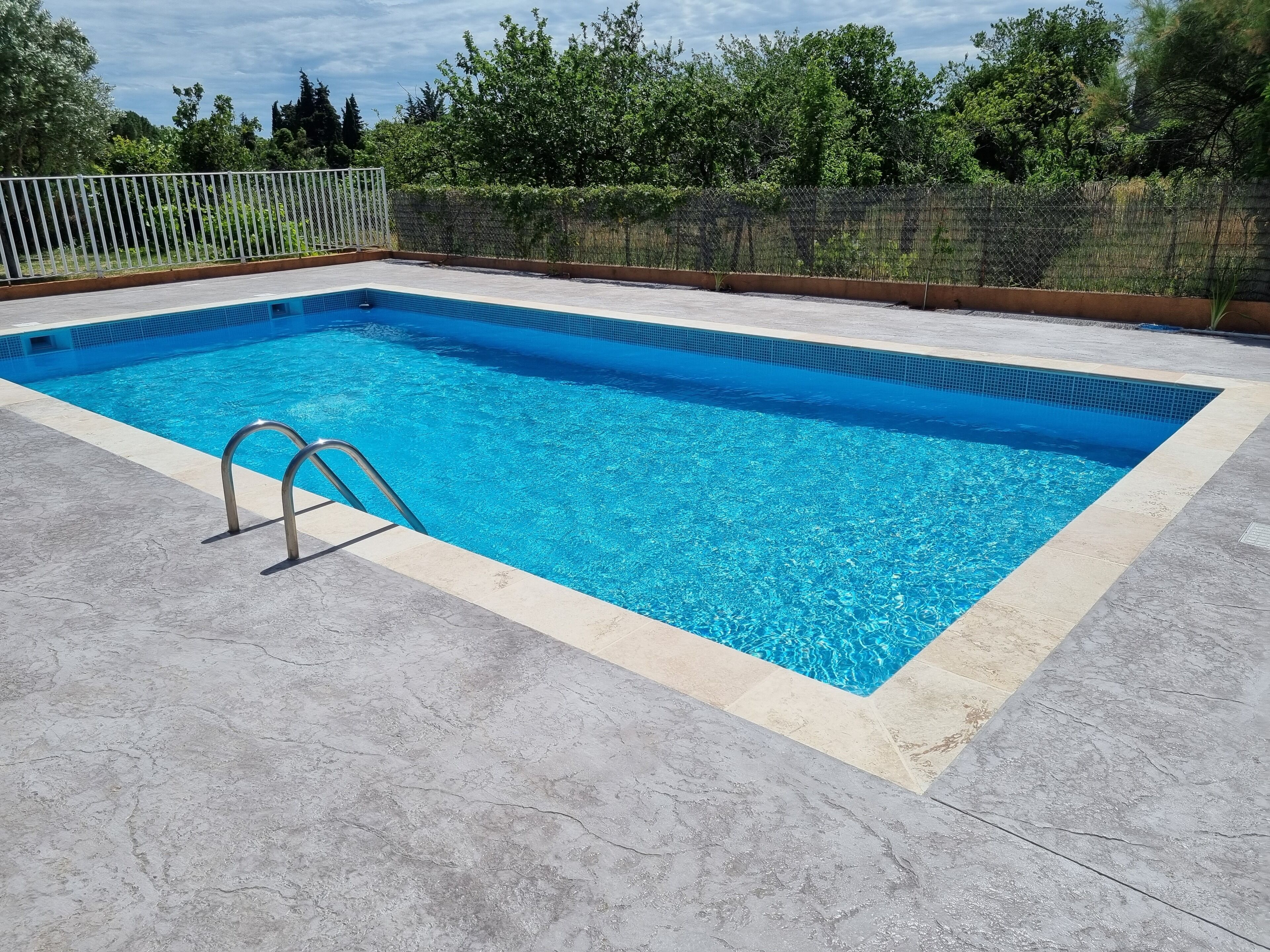A rectangular swimming pool with a metal ladder on one side, surrounded by a concrete deck.