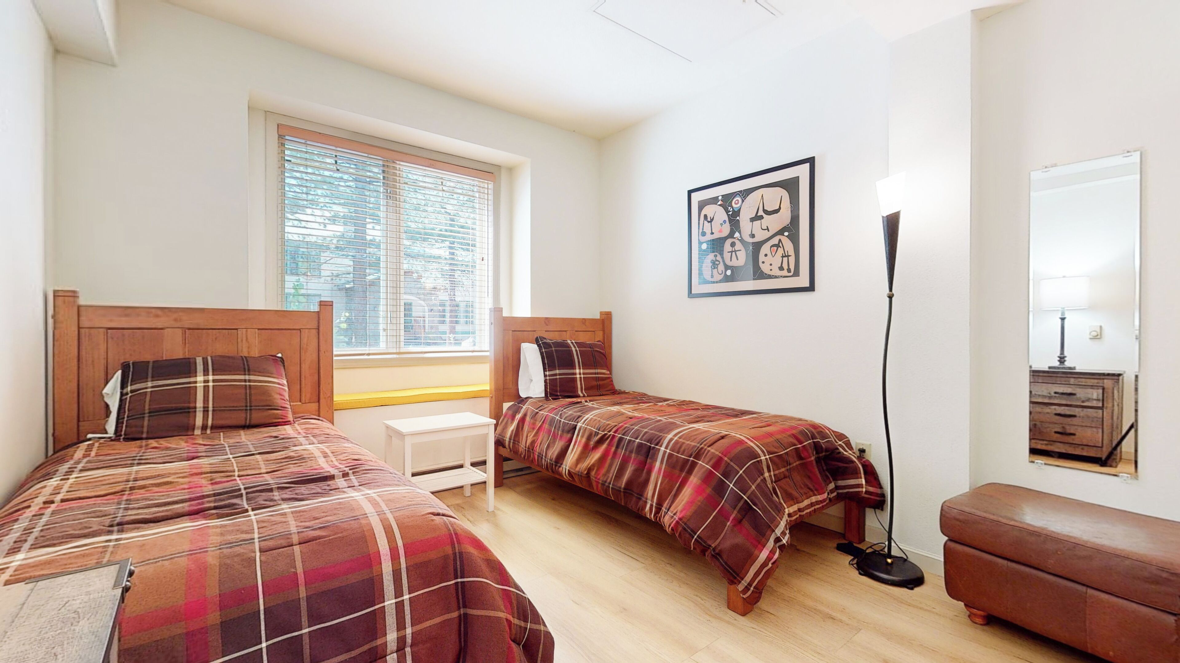 Een slaapkamer met twee bedden, een raam, een nachtkastje, een lamp, een kast en een spiegel.