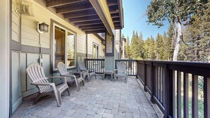 A covered patio with Adirondack chairs and a table, overlooking a forested area. - On Golf Course! Lovely Furnished, Private Gas Grill & Laundry. Pool On-site (Mammoth Lakes)