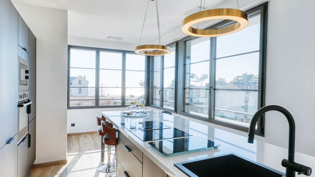 Une cuisine moderne dotée d’un grand îlot central, d’appareils électroménagers en acier inoxydable et de grandes fenêtres offrant une vue sur la ville.