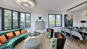Un salon moderne avec un canapé vert, une table basse ronde et un coin repas avec une table dressée pour six personnes.