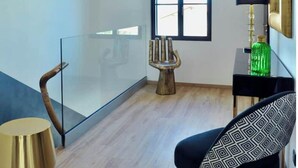 Une pièce moderne avec une cloison en verre, une chaise en bois, un canapé à motifs noir et blanc, une bouteille verte et une lampe posée sur une table noire.
