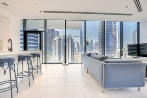 A modern living room with a large window, a sofa, a TV, and a bar area with stools.