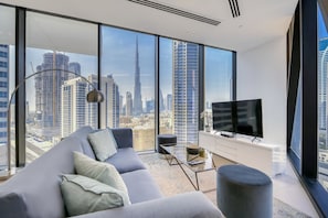 Ein modernes Wohnzimmer mit einer großen Couch, einem Couchtisch und einem Fernseher. Das Zimmer verfügt über große Fenster mit Blick auf eine Skyline mit hohen Gebäuden.