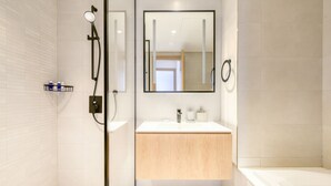 Un bagno moderno con cabina doccia in vetro, lavandino bianco con mobile contenitore in legno e una vasca da bagno ampia.