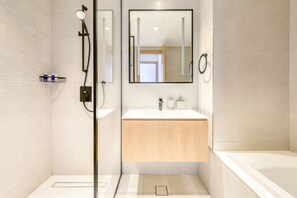 Une salle de bain moderne avec une douche à l’italienne en verre, un lavabo blanc avec un meuble-vasque en bois et une grande baignoire.