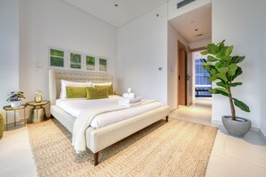 A modern bedroom with a large bed, a bedside table, a potted plant, and artwork on the wall.