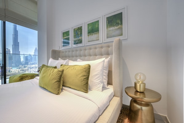 Ein modernes Hotelzimmer mit einem großen Bett, grünen und weißen Kissen, einem gepolsterten Kopfteil und gerahmten Kunstwerken an der Wand.