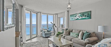 A spacious living room with a large window overlooking the sea, a cozy sofa set, a coffee table, and a telescope.