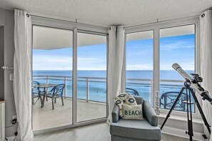 A balcony with a view of the ocean, a telescope, and a chair with a pillow labeled "BEACH".
