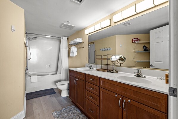 A bathroom with a shower, toilet, vanity with double sinks, and a large mirror.