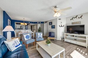 A living room with a blue sofa, striped chairs, a white coffee table, and a TV on a wooden stand.